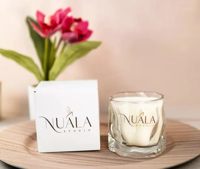Vela de Nuala Studio en vaso de vidrio junto a su caja con el logo, sobre una bandeja de madera